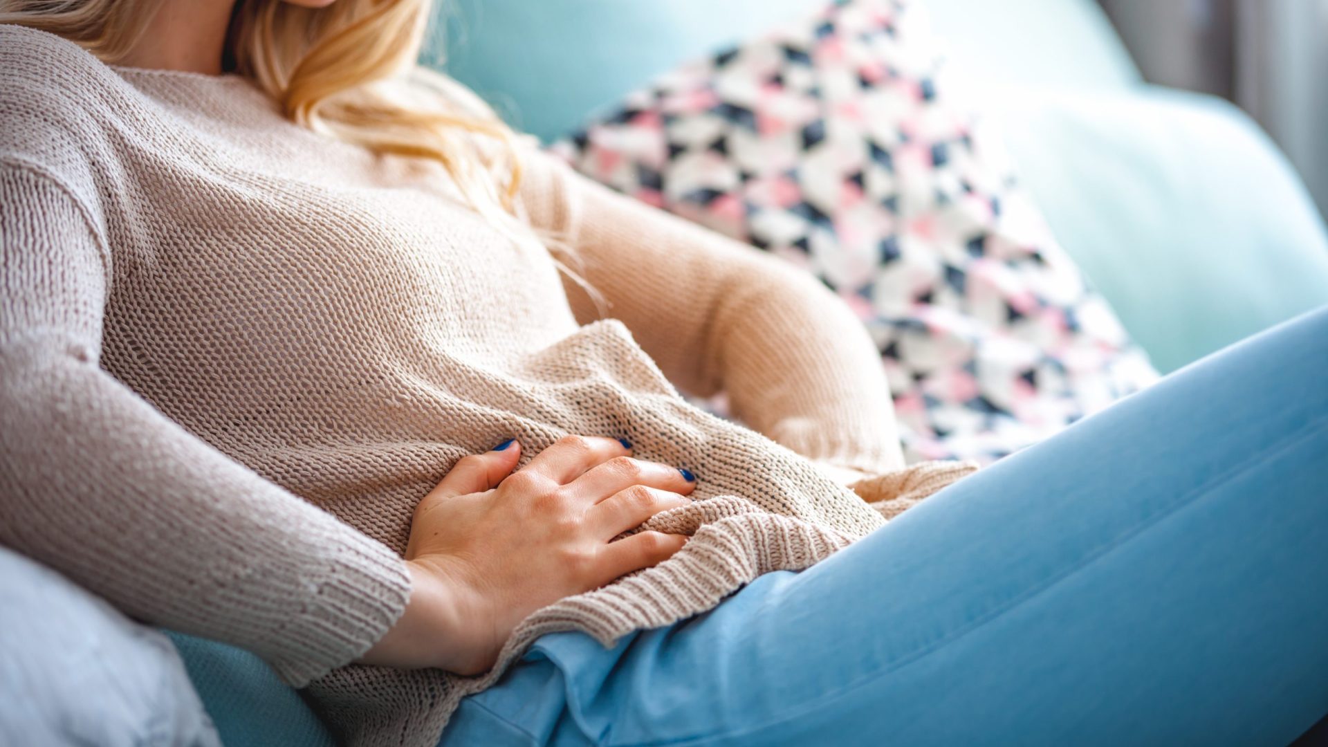 Young woman suffering from abdominal pain while sitting on sofa at home